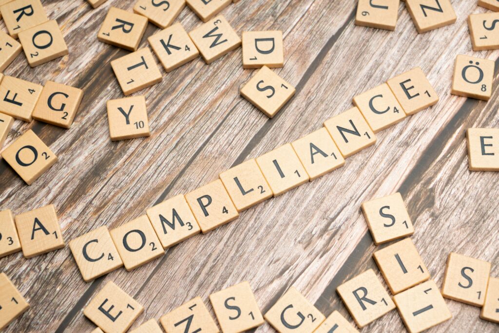 Scrabble tiles spelling "compliance" on a wooden surface, Government Compliance section.