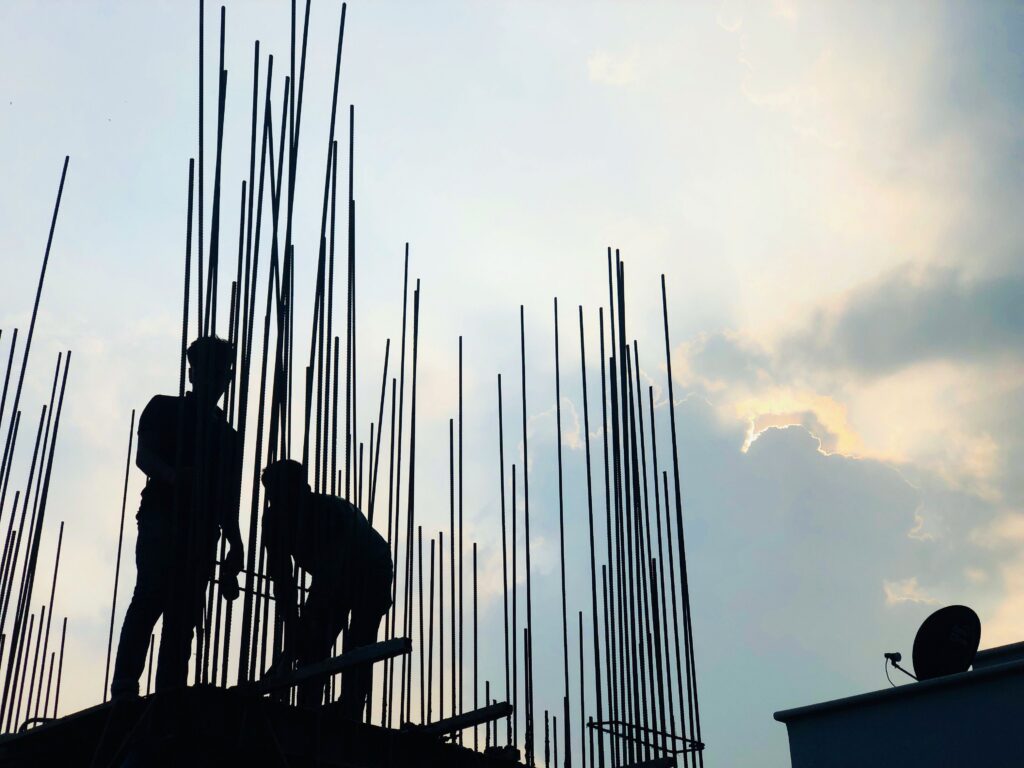 Silhouette of two construction workers among rebar rods at dusk.